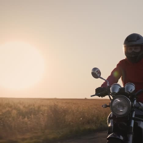 Die-Silhouette-Eines-Motorradfahrers,-Der-Bei-Sonnenuntergang-Auf-Einer-Landstraße-Fährt