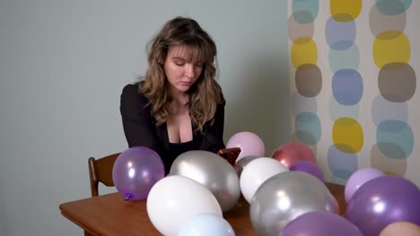 jeune femme assise à une table, regardant son téléphone, entourée de ballons