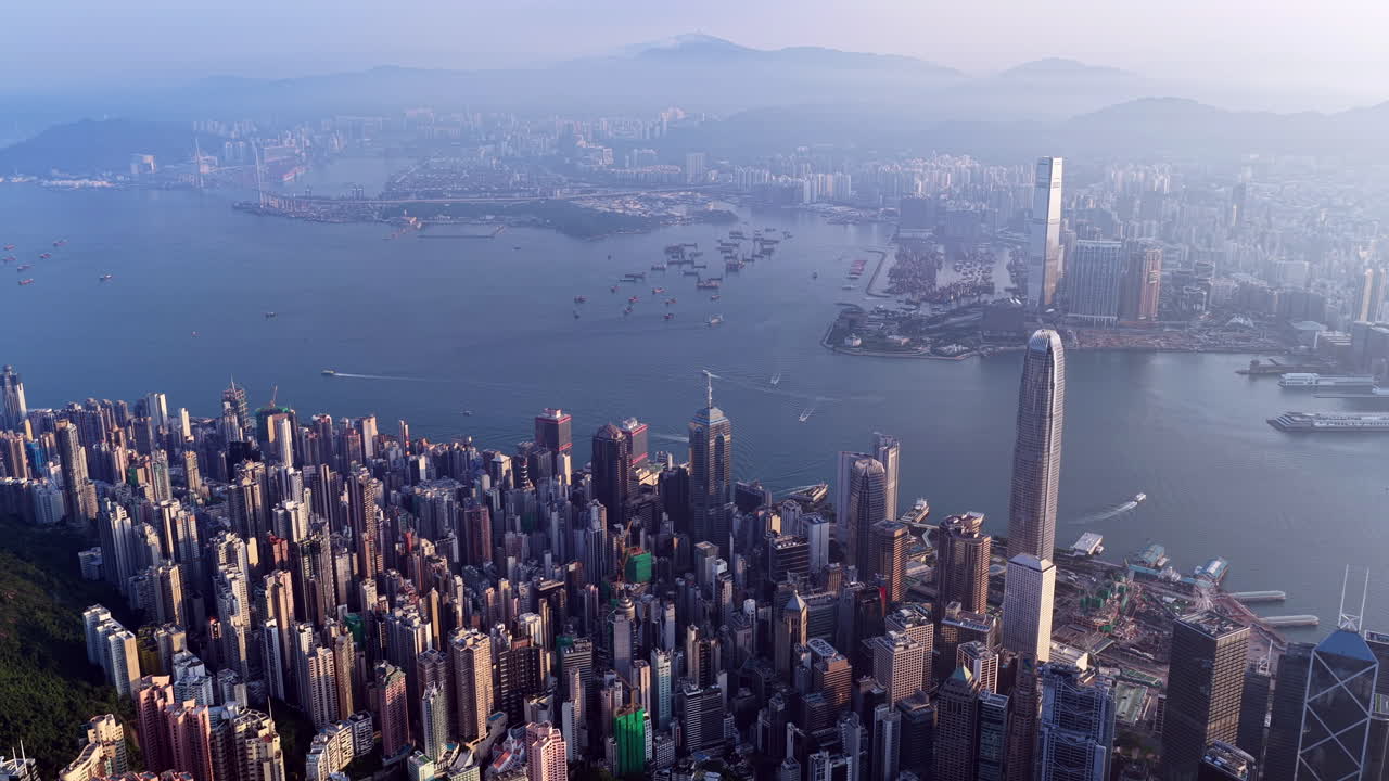 Cinematic aerial view of Hong Kong skyline shrouded in mist at blue hour, with glowing skyscrapers and Victoria Harbour fading into a moody, atmospheric twilight