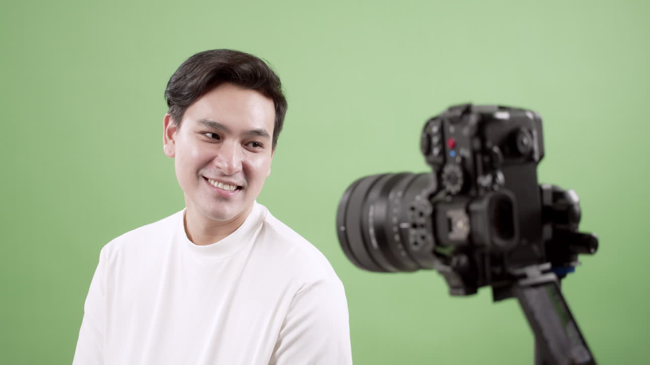 A joyful man poses for a video shoot against a vibrant green backdrop showcasing a lively atmosphere.