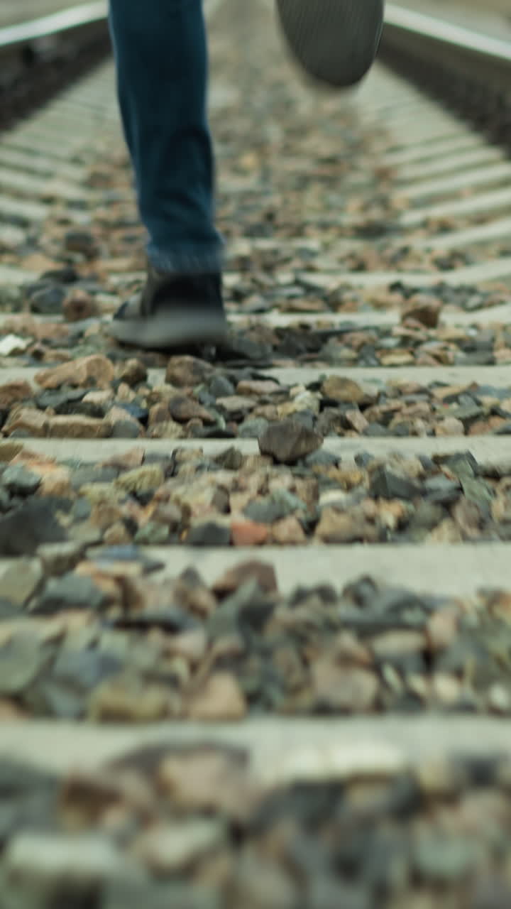 una vista de cerca de alguien corriendo en una vía ferroviaria, con pantalones vaqueros y zapatos de lona, la vía está cubierta de piedras con un borrón alrededor