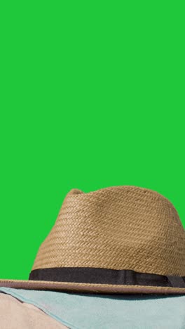 Vertical-Video-Summer-Holiday-Concept-Of-Sun-Hat-Mobile-Phone-Beach-Towel-On-Sand-Against-Green-Screen