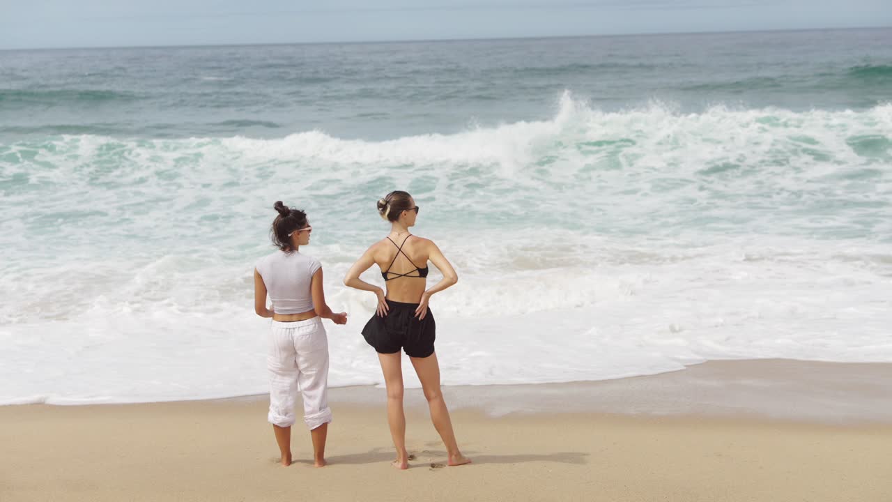 Two women standing on a beach looking at the ocean