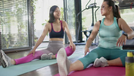amigas asiáticas felices estirándose y sonriendo en el gimnasio de casa soleado, cámara lenta