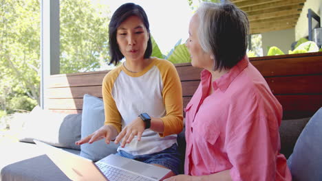 discussing health, asian woman explaining to senior asian woman using laptop on couch