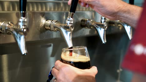 man pouring a pint of dark stout beer from a tap at restaurant happy hour