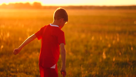 niño junior con una camiseta roja y zapatillas de deporte al atardecer haciendo malabarismos con un entrenamiento de pelota de fútbol y preparándose para convertirse en un jugador de fútbol. el camino hacia el sueño. trabajo duro