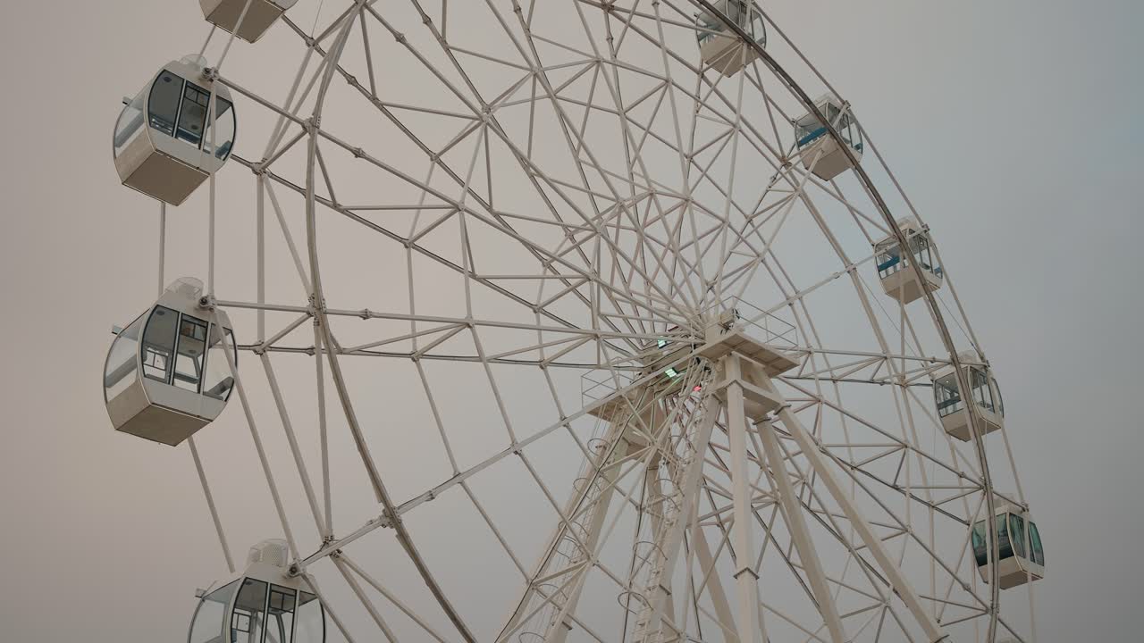 Ferris wheel against a pale sky, featuring glass-enclosed gondolas and a minimalist structure