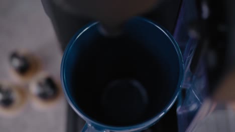 la mano pone una taza azul en una máquina de café moderna y vierte café, con cápsulas en el fondo, un ángulo alto de cierre con enfoque en rack