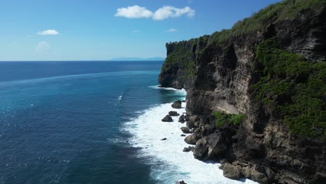 Los-Acantilados-De-Uluwatu,-Bali-En-Un-Caluroso-Día-De-Verano-Con-Olas-Rompiendo-Contra-Las-Rocas,-Antena