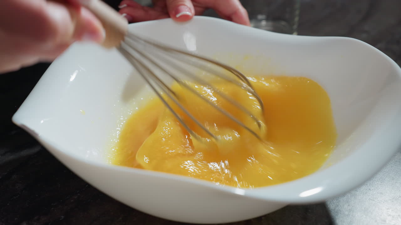 이 어두운 카운터 위에 색 그에 달을 휘두르는 클로즈업, 손잡이 나무 손잡이 휘두르기, 요리 또는 베이킹을 위해 부드러운 질감으로 노른자를 는, 달 혼합물이 빠르게 회전