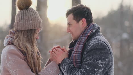 A-couple-in-love-a-man-warms-his-hands-with-his-breath-a-woman.-Stylish-couple-in-the-Park-in-winter-for-a-walk.