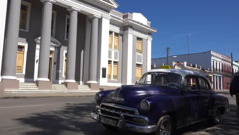 un gran edificio señorial se encuentra en la plaza central de cienfuegos, cuba, con un coche antiguo clásico en primer plano