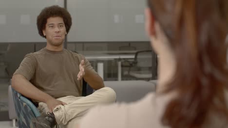 over the shoulder shot of african american male in his 20's in an office setting talking with a caucasian female in her 20's