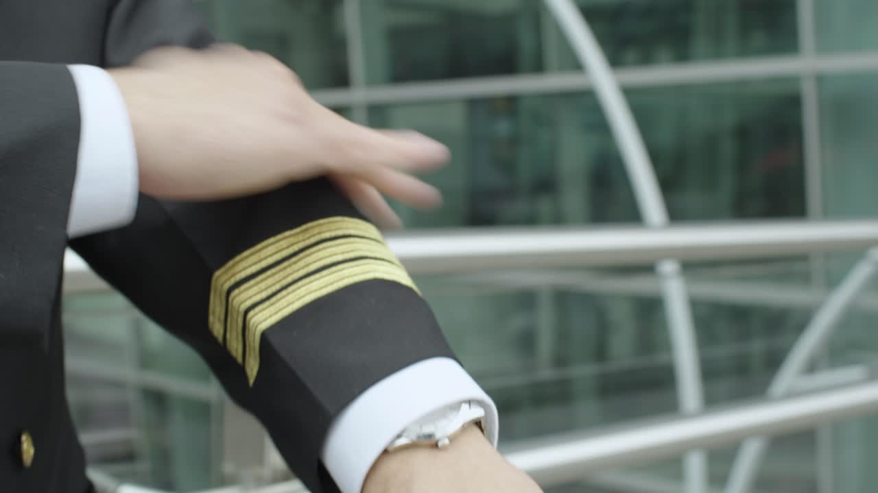 Close up of a stylish, unrecognizable gentleman's hands in formal wear buttoning up and adjusting his shirt sleeve at the airport. A pilot tightens his shirt sleeves before taking off.