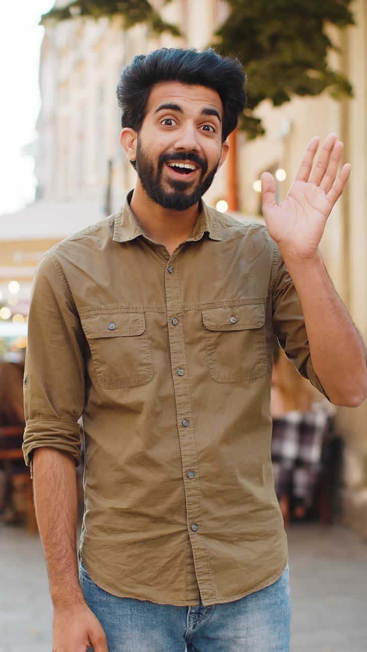 joven sonriendo amistosamente a la cámara agitando las manos hola hola saludo o adiós en la calle de la ciudad