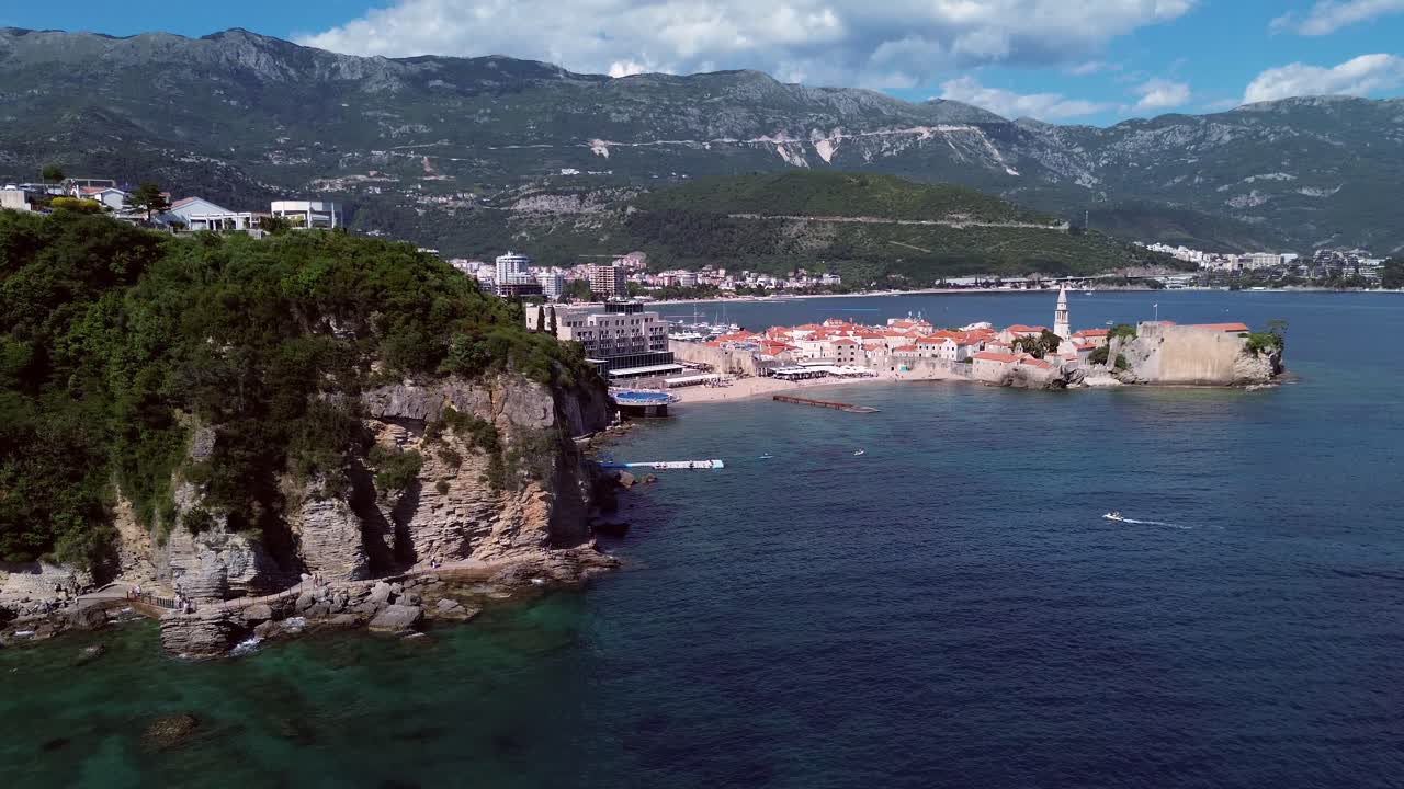 Crowded beach near old Budva town with old medieval fortress in view surrounded by Adriatic coastline and mountains, Aerial