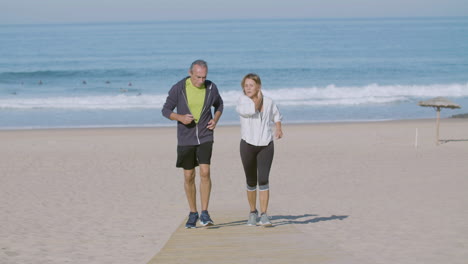 cheerful mature couple running uphill on sandy beach