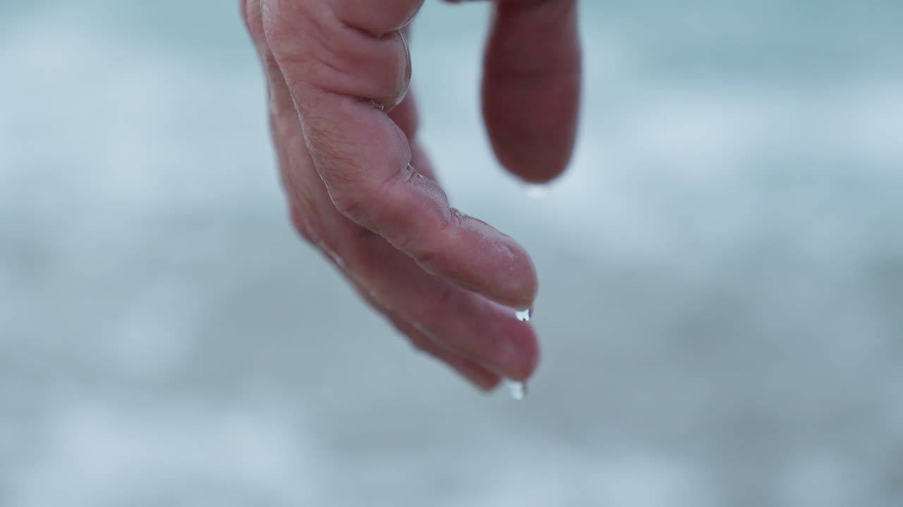 Close-Up of Water Dripping from Man's Hand on Grey Morning Beach