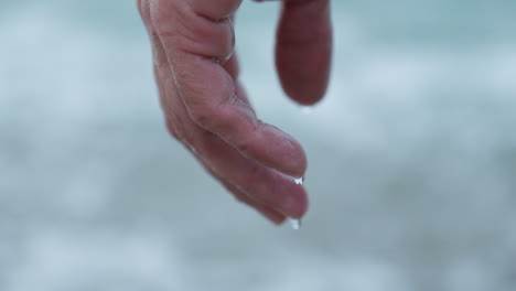 Nahaufnahme-Von-Wasser,-Das-Aus-Der-Hand-Eines-Mannes-Am-Grauen-Morgenstrand-Tropft