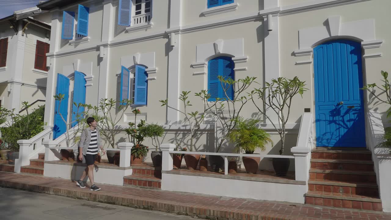 A person walking in front of a beautiful colonial building with blue doors and windows.