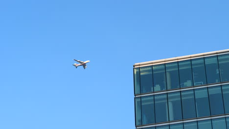 big passenger airplane flying over modern office building, low angle