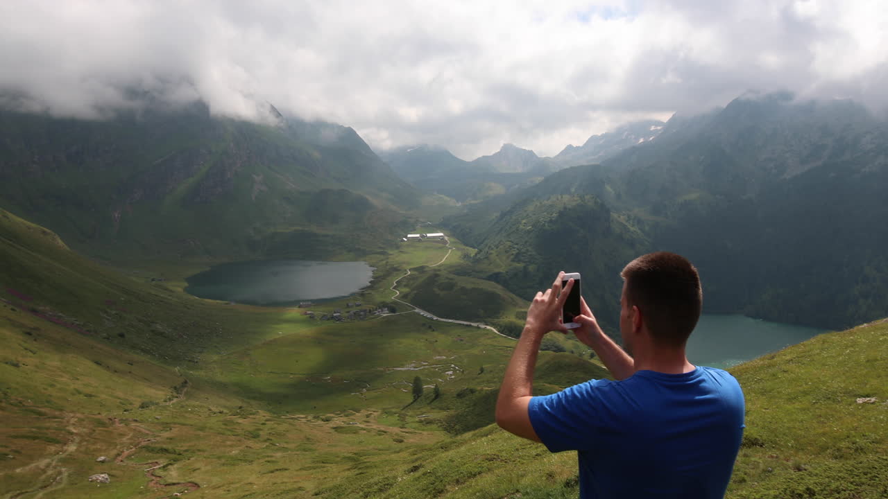 Young man taking a video of Lake Ritom in Switzerland with his mobile phone