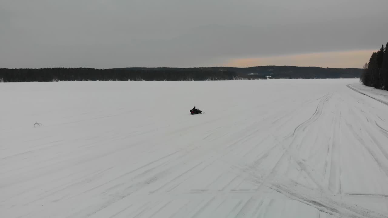 Tracking aerial shot of a man driving his snowmobile on Indalsalven in Timra, Sundsvall, Sweden.