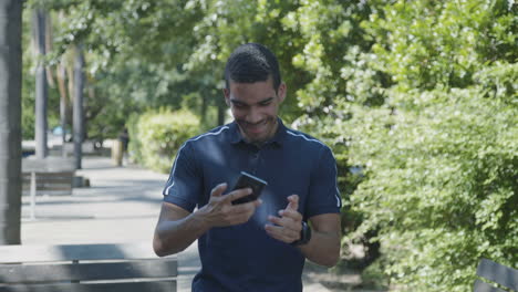 hombre enviando mensajes de texto por teléfono afuera, recibiendo buenas noticias, celebrando