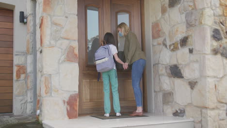 madre e hija con máscaras faciales abriendo la puerta de la casa