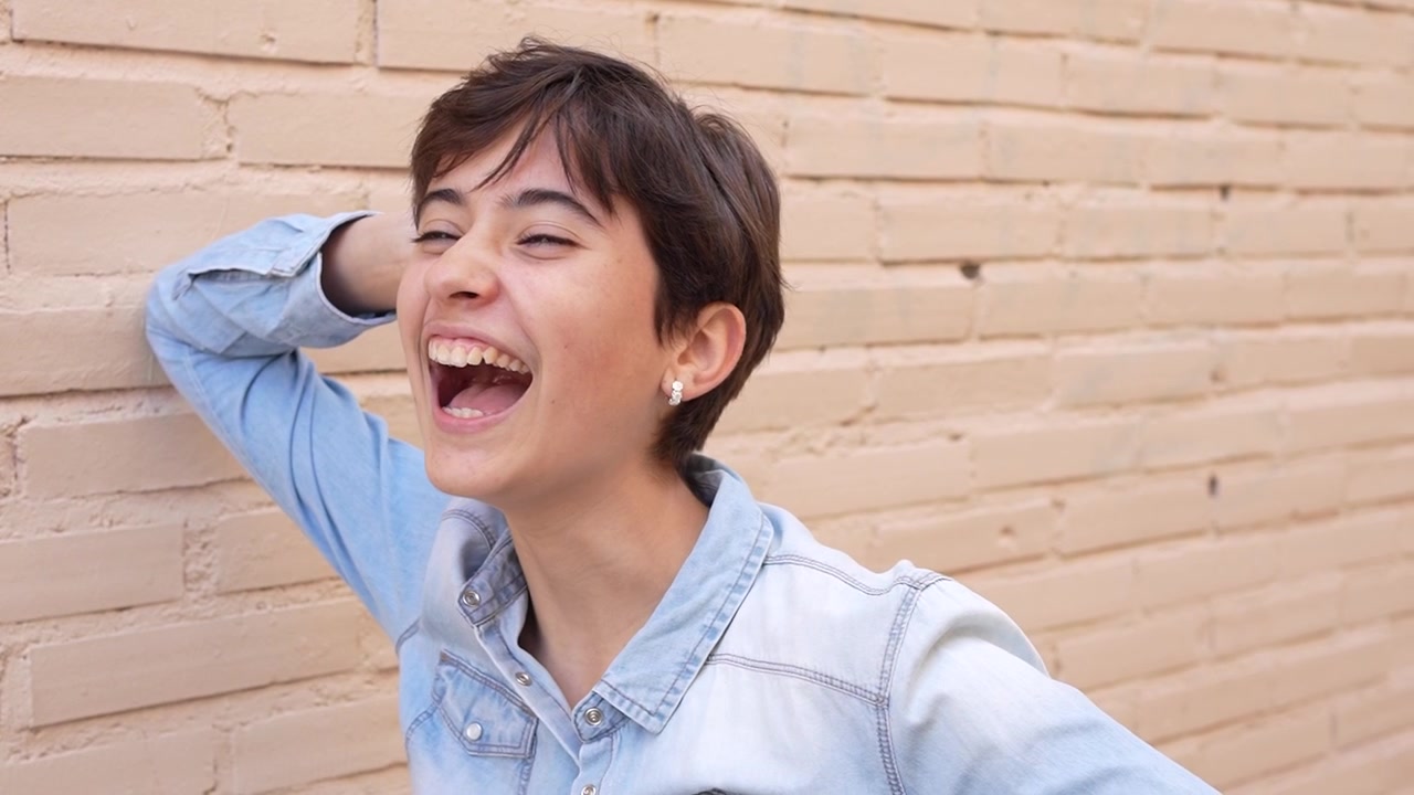 楽しそうな若い人が、レンガの壁を背景に輝くような笑顔を見せている。