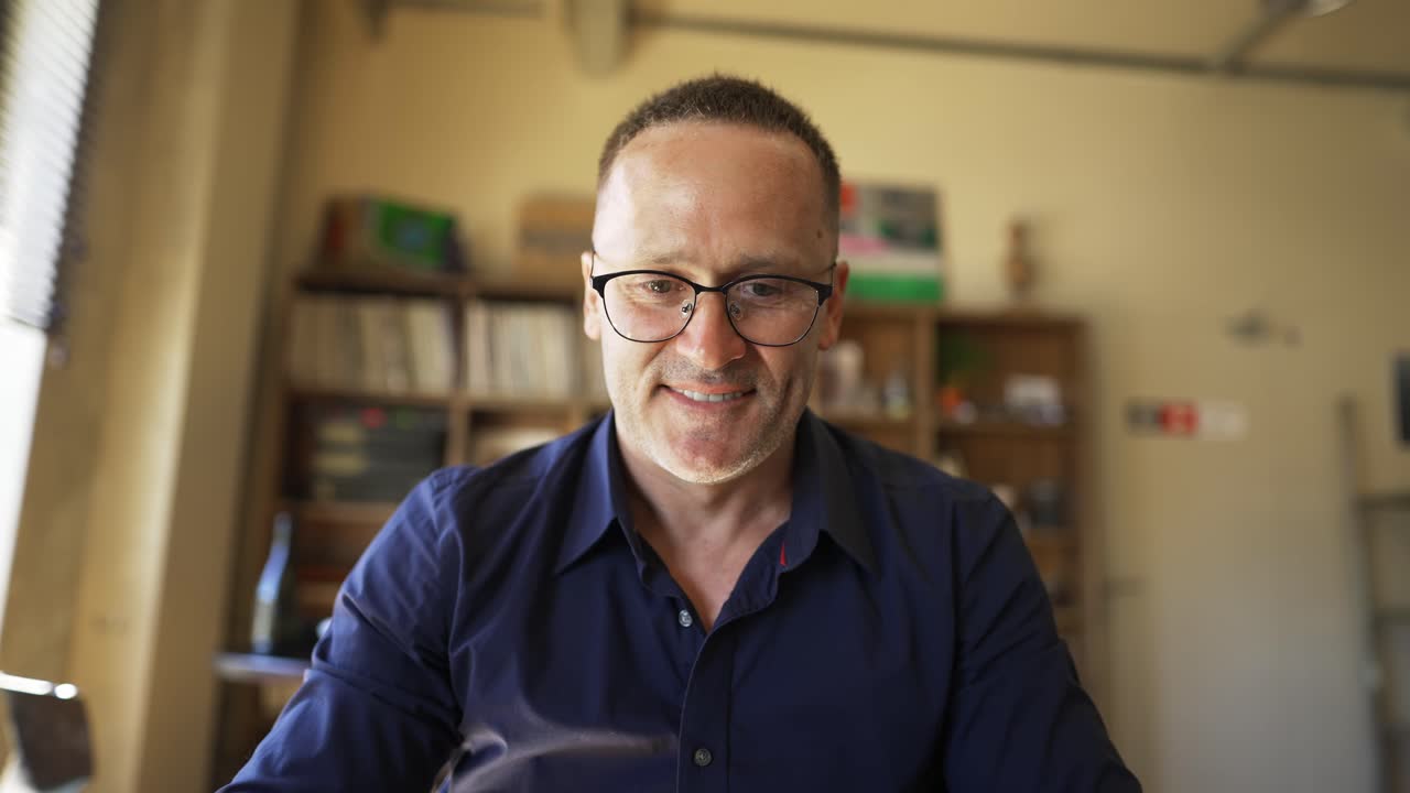 Adult man in glasses sits in front of a laptop and types