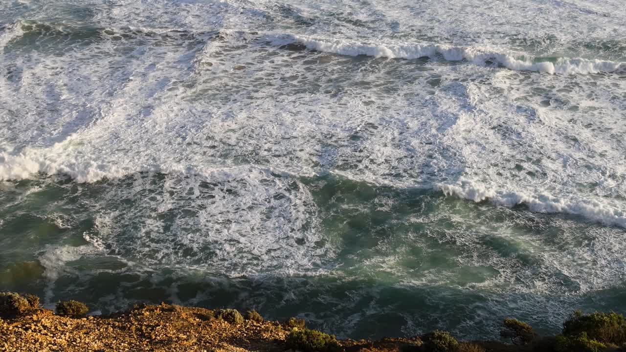 Close-up view of ocean waves crashing against a rocky shoreline, creating white foam and dynamic water patterns.