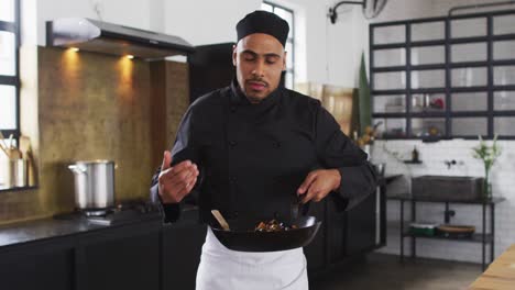 Mixed-race-male-chef-preparing-a-dish-and-smiling-in-a-kitchen-