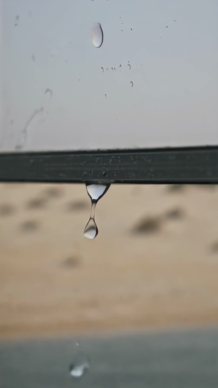 Close-up video of raindrops on a window with a blurred desert background