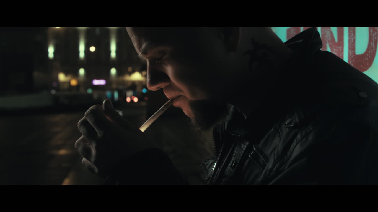 A bald dangerous looking man smoke outside a train station
