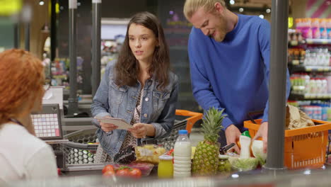 young couple laying out goods at the check out in a supermarket