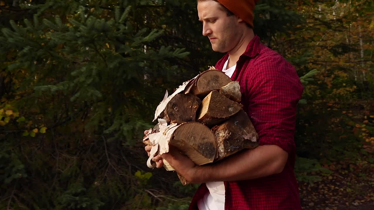 Handsome young man carrying a large pile of wood while camping in the beautiful countryside of Canada during the fall season