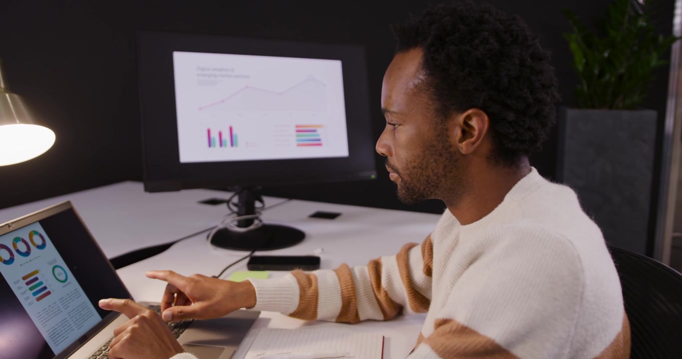 African American man turning to external monitor with charts, checking, updating laptop, copy space