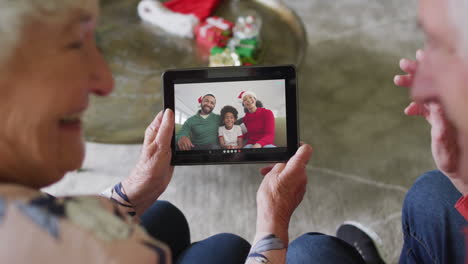 pareja caucásica mayor usando una tableta para una videollamada de navidad con una familia feliz en la pantalla