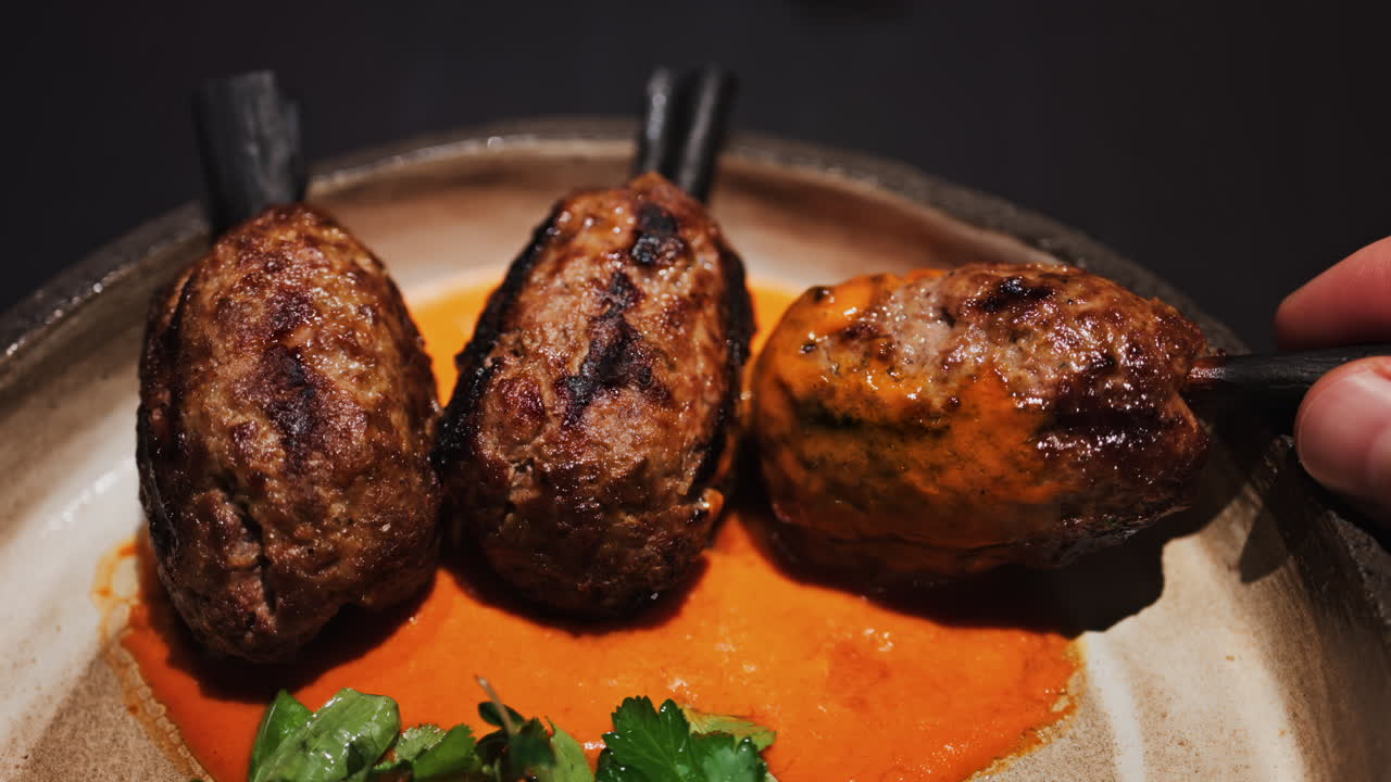 Three grilled meat skewers on charcoal sticks served on a plate with an orange sauce