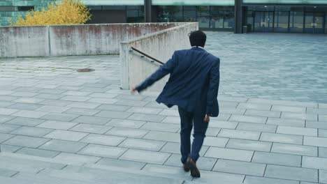 cheerful and happy businessman in a suit actively dancing while walking down the stairs. scene shot in an urban concrete park next to a business center. sunny day.