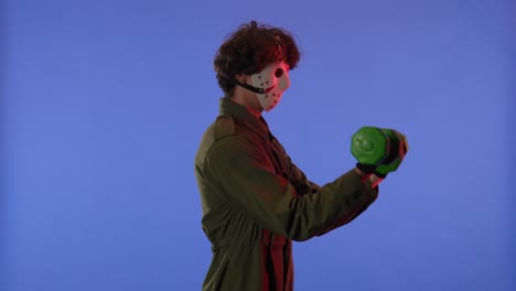 man in white mask swinging his arms with green dumbbells on blue background with red neon light