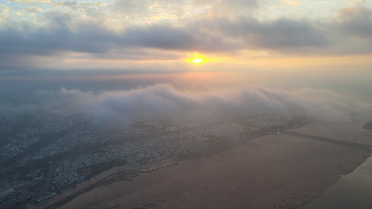 Sweeping aerial drone shot of Vijayawada at sunrise, showcasing the city and its surroundings partially covered in clouds.