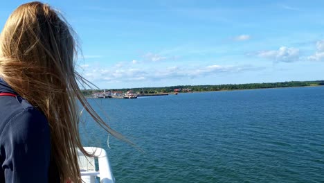 static view behind a blonde haired woman on a ship with her hair being blown about on a ferry crossing from uugu nature park to the mainland of estonia on the baltic sea