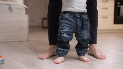 plano medio de un padre que ayuda a su bebé a ponerse de pie mientras pone un juguete en el suelo