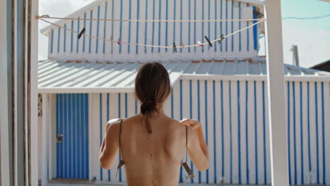 Chica-En-Topless-Quitándose-El-Sujetador-Del-Bikini-En-Casa-Verticalmente.-Mujer-Delgada-Colgar-Traje-De-Baño