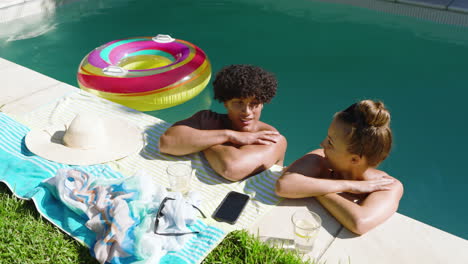 relaxing by pool, diverse couple enjoying sunny day with drinks and inflatable ring