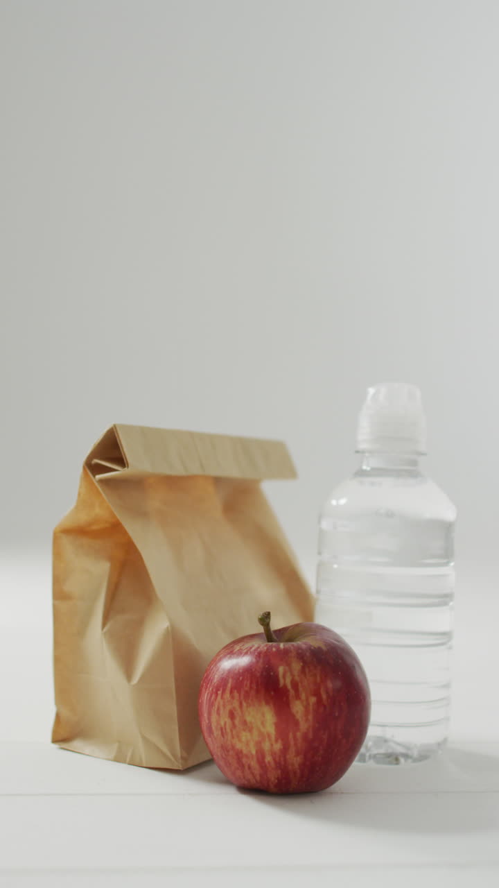 video vertical de almuerzo empacado en bolsa de papel con manzana y agua sobre fondo azul