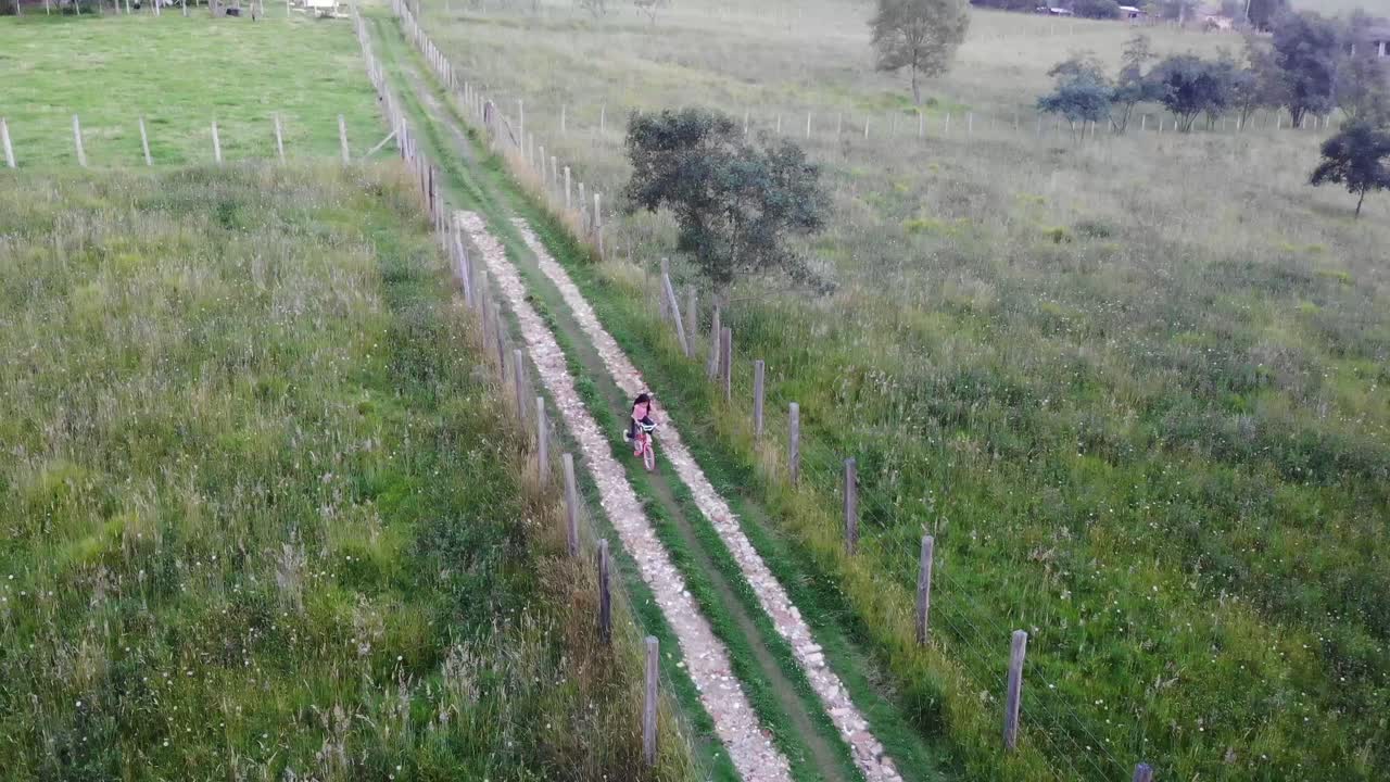 시골 길을 따라 자전거를 타는 어린 소녀의 공중 패닝 샷